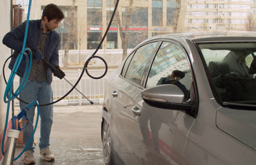 Handsome man washing car using high pressure washer. Self service on car wash.