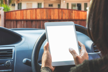 Woman inside car hand holding and using modern white digital tablet computer pc with blank screen  for content,text message and advertising with auto electric gate blur background.Clipping path.
