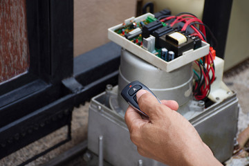 Technician man hand holding the  remote control, testing and checking the function of automatic gate. Maintenance concept.