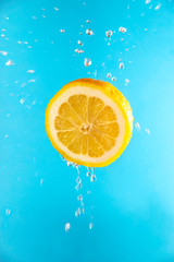 Fototapeta na wymiar Bright yellow lemon in flight with drops of juice on a blue background. The concept of lemonade and fresh sour juice for cooking.