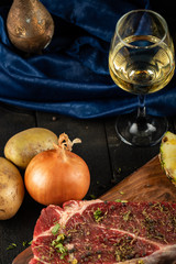 Raw meat on a wooden board with herbs and spices, served with a glass of wine