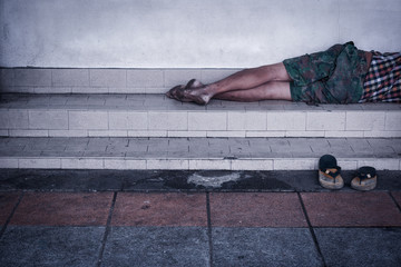 Homeless man dirty sleeps on the street in the shadow of the building.