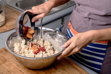Woman's hands putting dry fruits into flour while making homemade pastry.