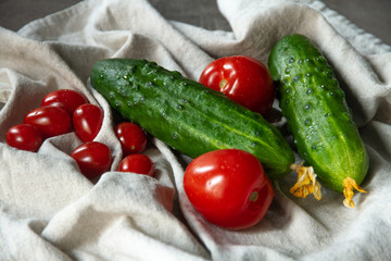 fresh vegetables tomatoes and cucumbers on 
linen cloth lying on grey table
