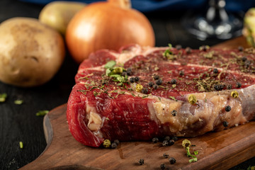Raw meat on a wooden board with herbs and spices, served with onion and potatoes