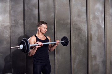 man in black sports uniform with dumbbells on a background of gray wall