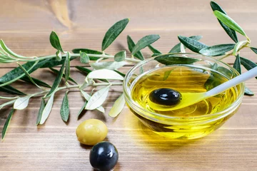 Foto op Plexiglas Black olive in spoon in olive oil. Some olives and olive tree branches on the wooden background in sunlights. © zveruga