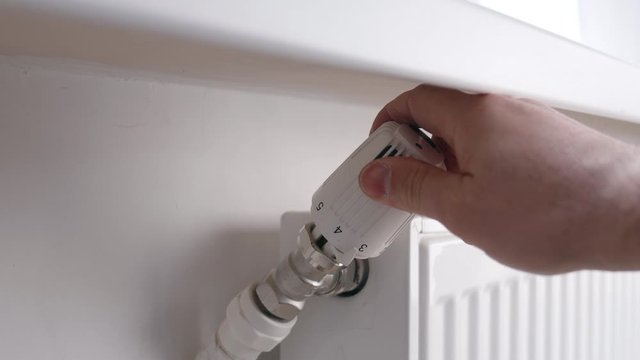 The male hand controls the heating of the white battery with the controller. White surroundings. The concept of heat and household chores.