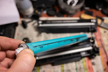 the fingers of a print repair technician hold the photoreceptor of a disassembled laser printer...