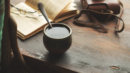 Cup of coffee, old book and glasses on the windowsill, near a chair with a plaid