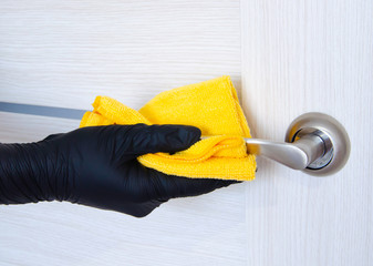 A female hand in a black glove cleans the door handles with a yellow napkin. The concept of the...