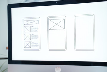 Web designer at work. Graphic designer. Mobile application design. Designer desktop. UX, UI design. Thumbnails of a mobile application on a computer screen. Gadgets, sketchbook and phone on the table