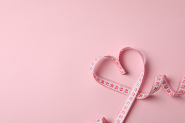 Measuring tape in the form of heart on pink background