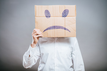Putting a smiling face on. Man holding cardboard paper with smiley face printed on as sadness...