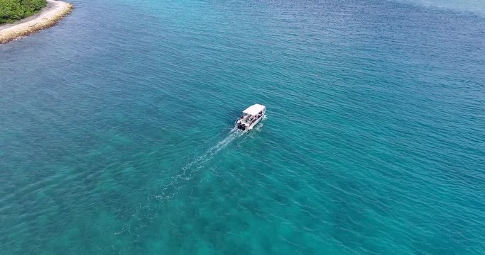 Stunning drone tracking shot of a speed boat in the Tuheiava Pass in paradise island Tikehau, French Polynesia. A small beach with palm trees and pink sand and turquoise blue water of South Pacific