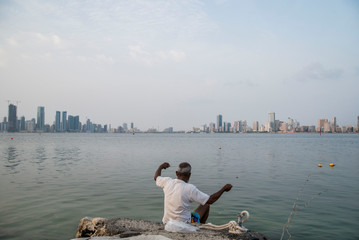 man fishing in front of manama bahrain skyline