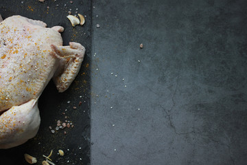 Whole raw chicken with spices on dark background. Top view with copy space.