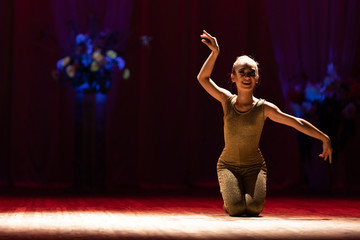 Young girl gymnast performs with a performance on stage in a theater