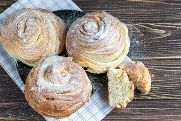 Bakery products with raisins and dried fruits are located on a dark wooden background. Sprinkled with icing sugar. Kraffins. Easter food.