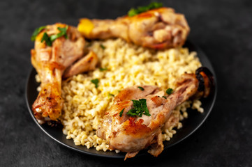 grilled chicken legs with spices on a plate and cooked bulgur on a stone background