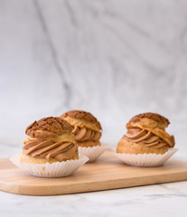 Homemade choux cream or cream puffs with tea cream on wooden background.