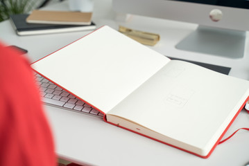 Web designer at work. Graphic designer. Girl in red dress with red sketchbook. Designer desktop. Gadgets, display, sketchbook and phone on the table
