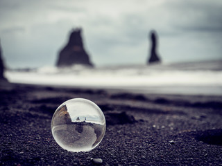 Cold sea water rolling on wet sand near rough stony cliffs on stormy day on Reynisfjara Black Beach in Iceland