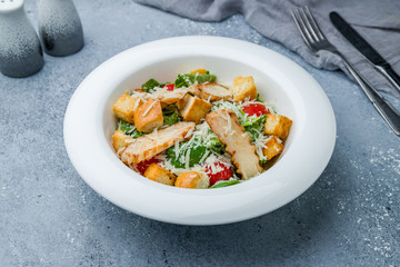 Salad caesar with chicken on white plate on grey table
