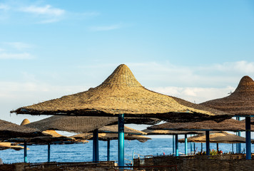 Straw beach umbrellas with the Red Sea and blue sky with clouds on the background. Marsa Alam, Egypt, Africa.