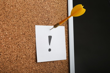 paper with exclamation mark pinned to a cork board by a dart