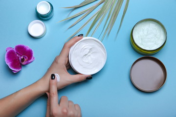 woman's hand takes some cream from a jar. Moisturizing cream in woman's hands on blue background with cosmetic jars flat lay.