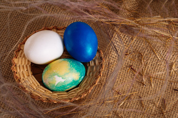 Fototapeta na wymiar Colorful Easter eggs white and blue colors in a wicker basket on a brown cloth background. Close up