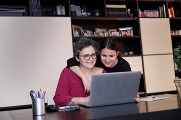 Madre e figlia si abbracciano affettuosamente davanti al computer a casa 