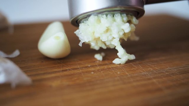 Anonymous female hands crushed fresh garlic in the metalic masher on wooden tabletop for increased immunity. Healthy food for fighting viruses. Concept of coronavirus or COVID-19 pandemic Close up
