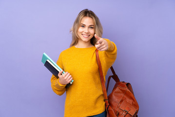 Teenager Russian student girl isolated on purple background pointing to the front and smiling
