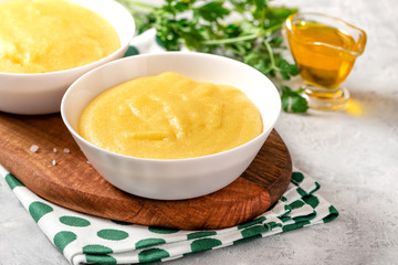 Traditional cooked polenta in a white bowl on a gray concrete table. Italian food.