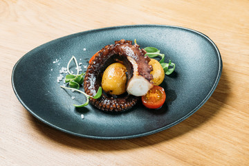 grilled octopus tentacles, served with potatoes and vegetables tomatoes on a blue plate © dobrovizcki