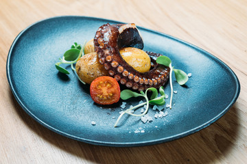 grilled octopus tentacles, served with potatoes and vegetables tomatoes on a blue plate