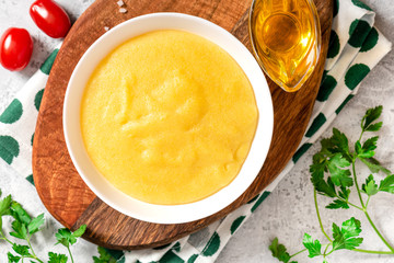 Traditional cooked polenta in a white bowl on a gray concrete table top view. Italian food.