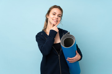 Fototapeta premium Teenager Russian girl holding mat isolated on blue background smiling