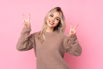 Teenager blonde girl wearing a sweater over isolated pink background showing victory sign with both hands