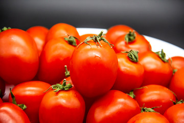 Ripe fresh red cherry tomatoes on a white plate against dark background.  Beautiful and healthy fresh cherry tomatoes without GMO.