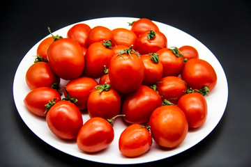 Ripe fresh red cherry tomatoes on a white plate against dark background.  Beautiful and healthy fresh cherry tomatoes without GMO.