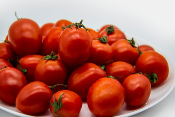 Ripe fresh red cherry tomatoes on a white plate against white background.  Beautiful and healthy fresh cherry tomatoes without GMO.