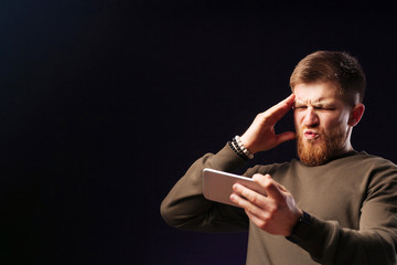 Upset shocked bearded man, holding smartphone watch devastating news or video, punch forehead,...
