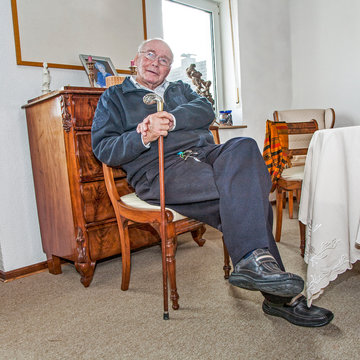 old man enjoys sitting in the living room with hands on walking stick