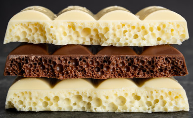 broken pieces of textured porous chocolate, white and milk, closeup background