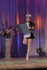 A young girl ballerina in a school uniform with an alphabet book in her hands dances a ballet performance on stage in a theater on a red background © Kozlik_mozlik