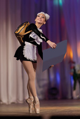 A young girl ballerina in a school uniform with an alphabet book in her hands dances a ballet performance on stage in a theater on a red background © Kozlik_mozlik