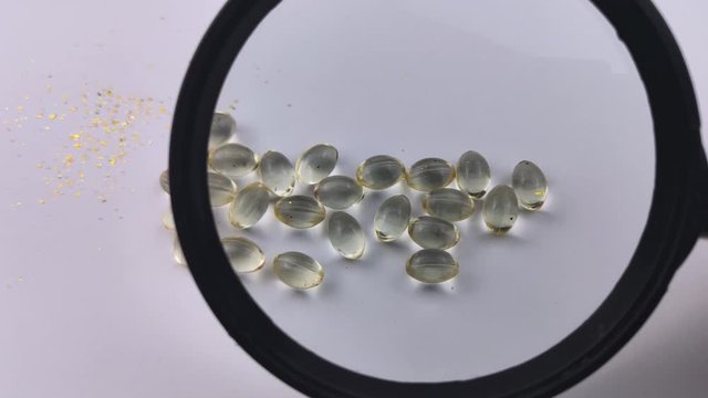 A person examines vitamin D3 capsules under a magnifying glass. A magnifying glass passes over the capsules making them large. Health Care Concept